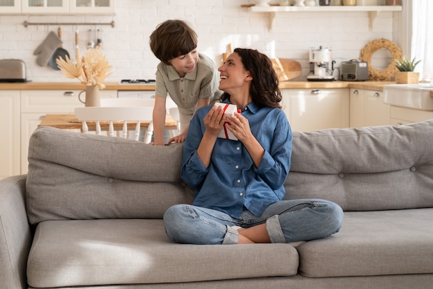 Un petit fils fait une surprise d'anniversaire à maman saluant une mère avec la fête des mères en lui donnant une boîte-cadeau