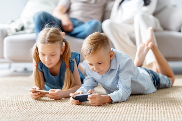 Petit frère et soeur jouant à des jeux divertissants sur leurs smartphones