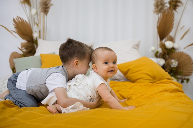 Le petit frère et la soeur jouent sur une couverture en laine jaune sur le lit de la chambre