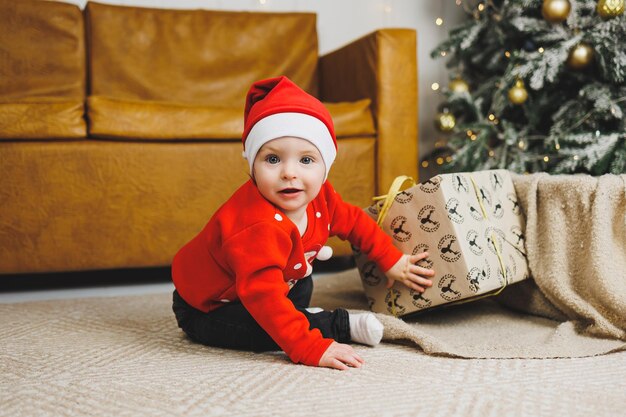Un petit garçon de 1 an est assis dans un panier sur fond d'arbre de Noël Un enfant dans un vent rouge du Nouvel An près de l'arbre de Noël