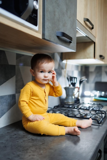 Un petit garçon de 1 an en vêtements jaunes est assis dans la cuisine sur la table Portrait d'un mignon garçon d'un an