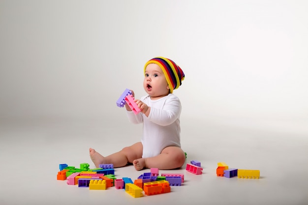 Petit garçon de 9 mois jouant avec un constructeur multicolore sur un mur blanc