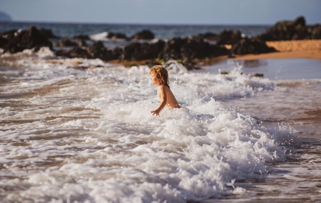 Petit garçon actif éclaboussant dans les vagues de la mer un jour d'été pendant les vacances le concept de fami