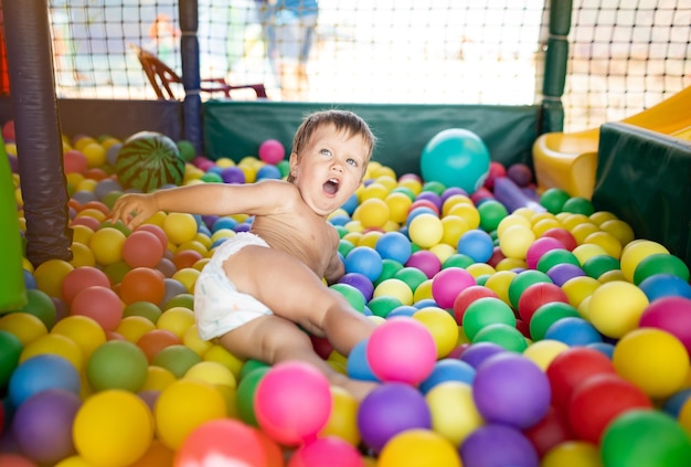 Un petit garçon amusant et joyeux dans une couche avec une balle gonflable à rayures vertes dans ses mains joue dans la salle de jeux le week-end, profitant des journées d'été chaudes et lumineuses