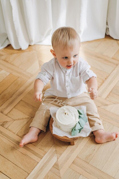 Un petit garçon d'un an lors de sa première séance photo de smash de gâteau mangeant un gâteau blanc de bento avec ses mains