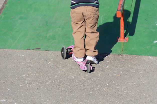 Un petit garçon apprend un sport extrême en faisant du scooter en été sur l'aire de jeux du parc et à l'extérieur