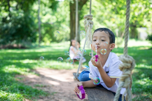 Photo un petit garçon asiatique faisant des bulles, jouant avec joie et bonheur dans la nature belle et verte.