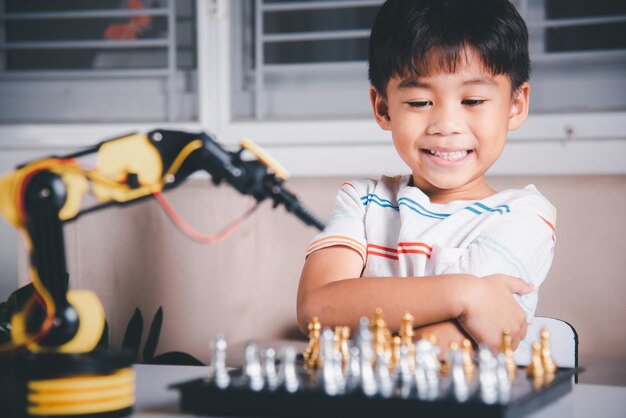 Le petit garçon asiatique joue aux échecs avec le bras de machine de robot