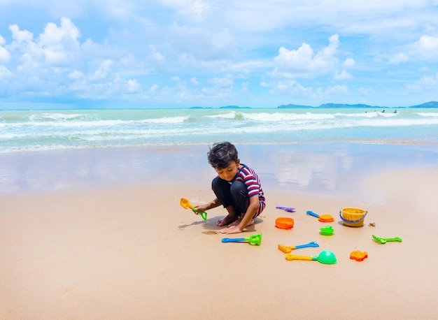 Petit garçon asiatique joue avec du sable sur la plage.