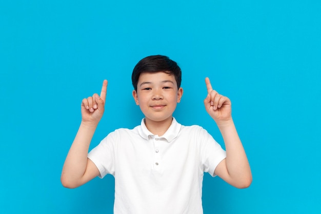 Un petit garçon asiatique montre ses mains sur un fond bleu. Un enfant coréen fait de la publicité pour un espace de copie.