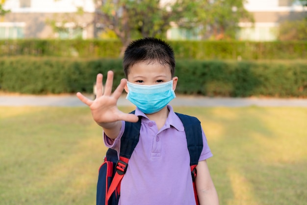 Petit garçon asiatique portant un masque pour protéger pm2.5 et montrer un geste d'arrêt des mains pour arrêter l'épidémie de virus corona.