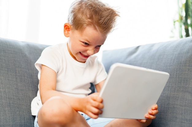 Petit garçon assis sur un canapé et à l'aide de tablette numérique à la maison, portrait