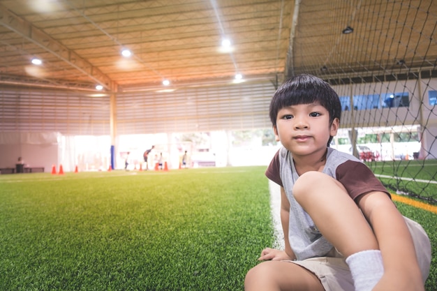 Petit garçon assis dans le champ de train de sport de football