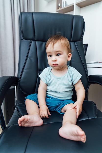 Un petit garçon assis dans un grand fauteuil en cuir noir Petit bébé patron