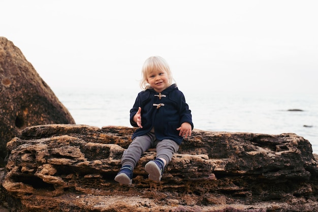 Petit garçon assis sur la falaise près de la mer en automne ou en été