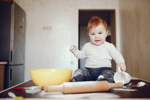 petit garçon assis à la maison sur une table dans la cuisine près d&#39;une assiette de farine