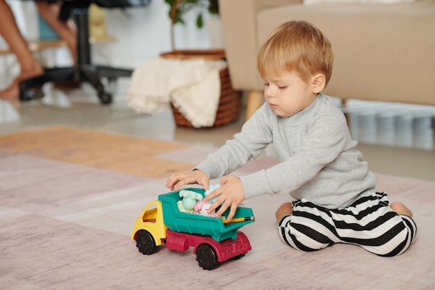 Petit garçon assis par terre et jouant avec sa petite voiture dans la chambre