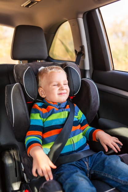 Petit garçon assis sur un siège d'auto attaché dans la voiture.
