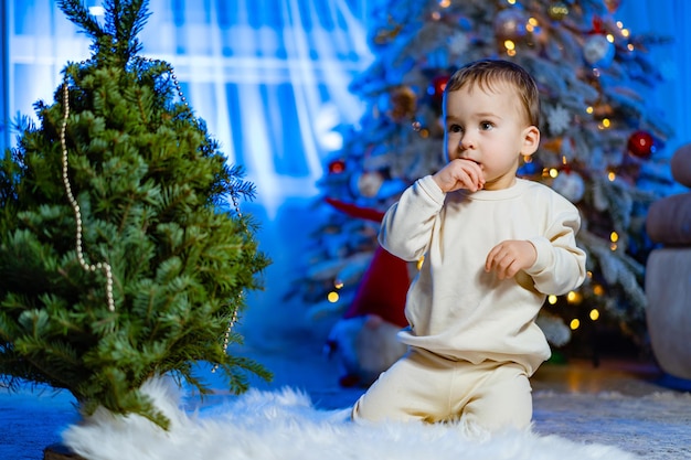 Petit garçon assis sur le sol près de l'arbre de Noël Joyeux et lumineux Noël