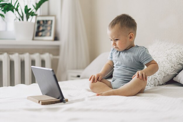 Petit garçon assis avec une tablette dans la chambre