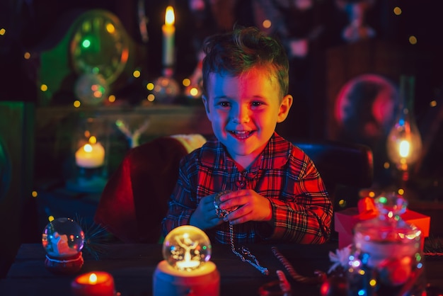 Un petit garçon, l'assistant du Père Noël, est assis à une table avec des cadeaux dans de fabuleuses décorations de Noël. Carte postale.