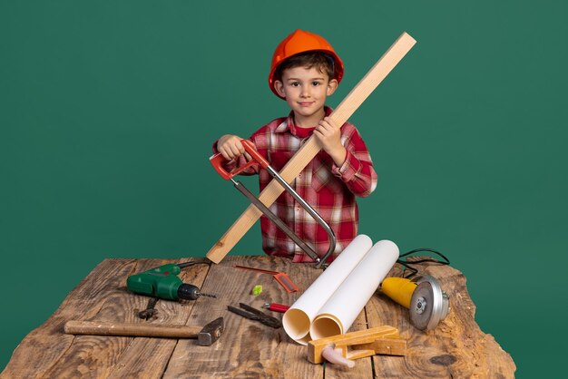 Petit garçon au chapeau de constructeur tenant une scie sur bois