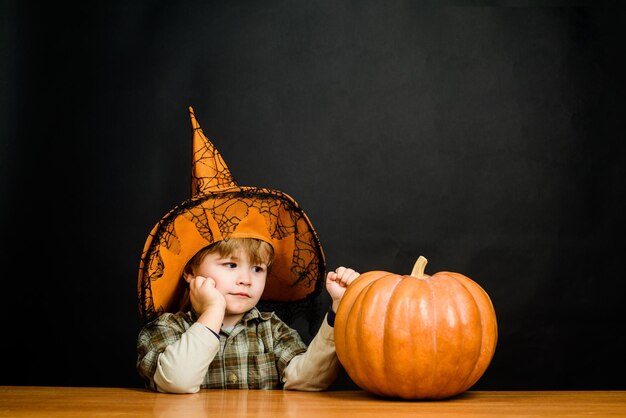 Petit garçon au chapeau de sorcière avec citrouille d'halloween. Citrouille d'Halloween. Préparation pour Halloween. Garçon habillé tour ou traitement. Enfant à la citrouille. Vacances d'Halloween. La charité s'il-vous-plaît. Joyeux Halloween.