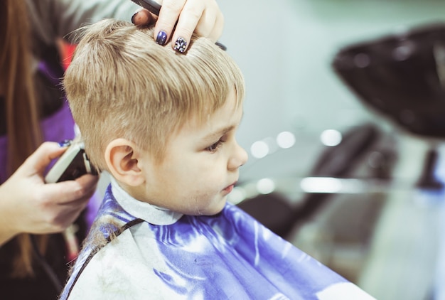 Photo petit garçon aux cheveux blonds coupés dans un salon de coiffure à l'aide d'une machine