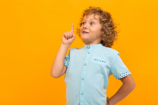 Petit garçon aux cheveux bouclés en chemise bleue et short a une excellente idée isolée sur jaune