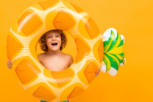 Petit garçon aux cheveux bouclés en maillot de bain avec grand cercle en caoutchouc isolé sur fond jaune