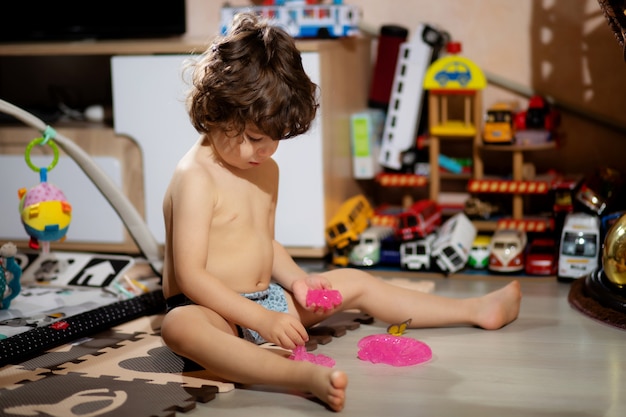 Photo le petit garçon aux cheveux bouclés en short joue avec de la boue dans sa chambre, pour ne pas salir ses vêtements.