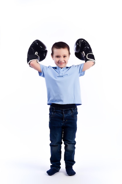 Un petit garçon aux cheveux noirs en jeans bleu un polo bleu en gants de boxe noir et blanc