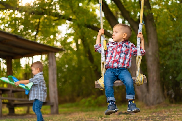 Petit garçon sur une balançoire dans un parc verdoyant. Enfance heureuse.