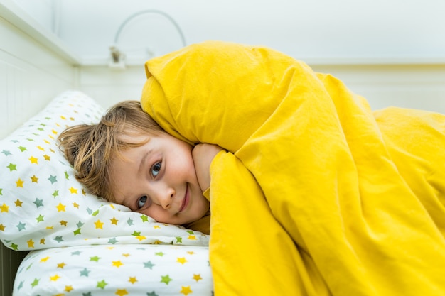 Petit garçon en bas âge est couché dans son lit. Enfant se réveillant le matin avec le sourire. Heureux enfant au repos à la maison.