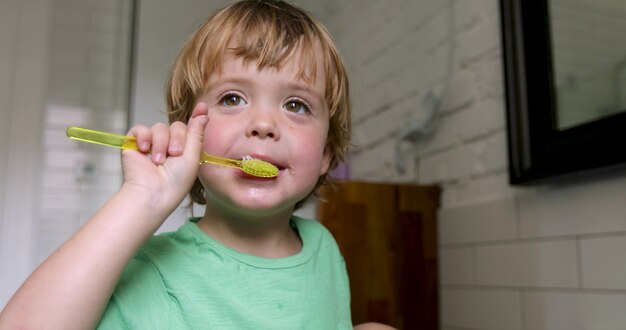 Petit garçon blond apprenant à se brosser les dents dans un bain domestique.