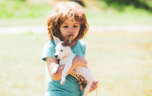 Petit garçon blond bouclé doux avec un chiot blanc sur des chiots de mains et un enfant en plein air