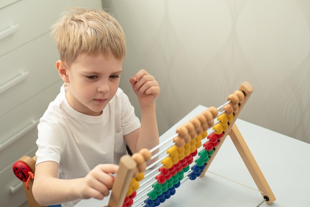 Photo petit garçon blond est engagé avec des factures en bois il se concentre sur les jeux montessori concept education