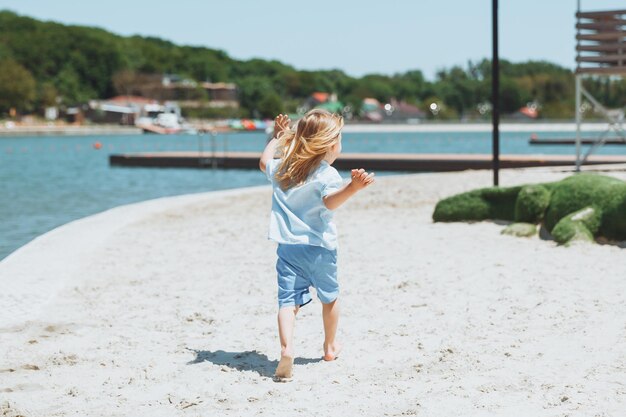Petit garçon blond heureux court et s'amuse sur la plage