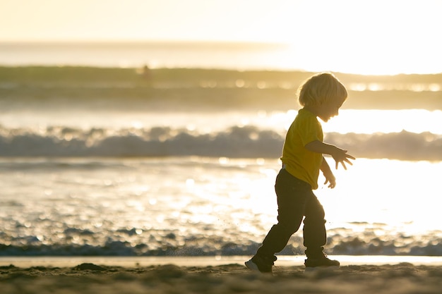 Petit garçon blond marchant sur la plage au bord de l'océan