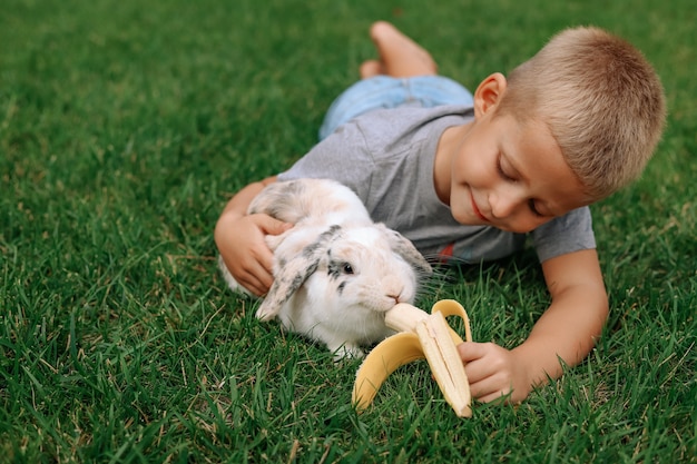 Un petit garçon blond nourrit un lapin aux oreilles tombantes.