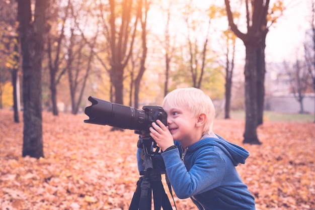 Petit garçon blond prend des photos sur un appareil photo reflex. Parc d'automne