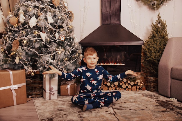 Un petit garçon blond rit et joue sur fond d'arbre de Noël.