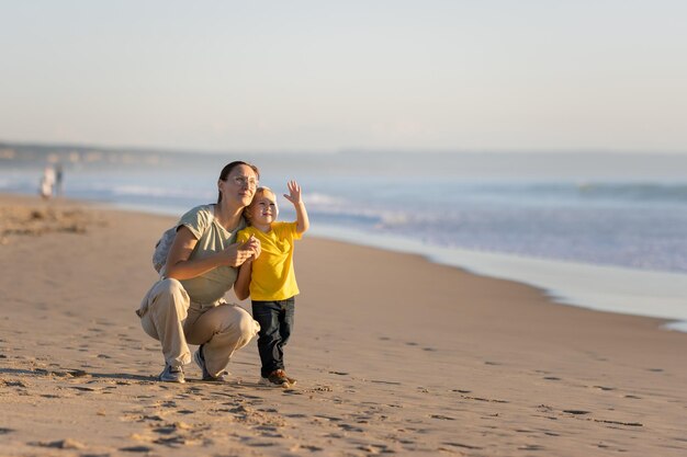 Petit garçon blond et sa mère marchant sur la plage au bord de l'océan et regardant le ciel