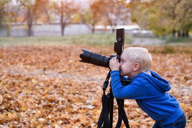 Petit garçon blond tire avec un grand appareil photo reflex sur un trépied