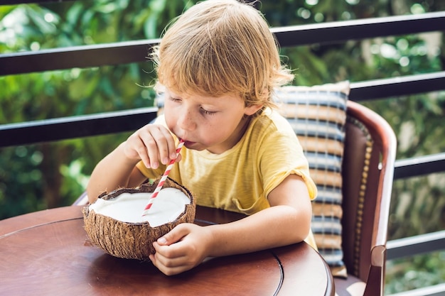 Le petit garçon boit du lait de coco fait maison à partir d'une moitié de noix de coco.