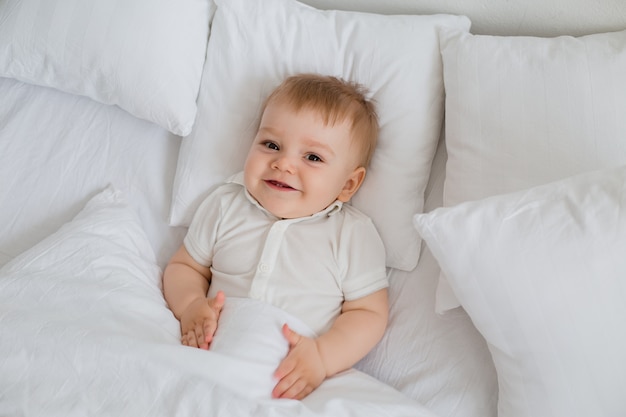 Petit garçon en bonne santé sourit en body blanc se trouve dans son lit avec du linge blanc