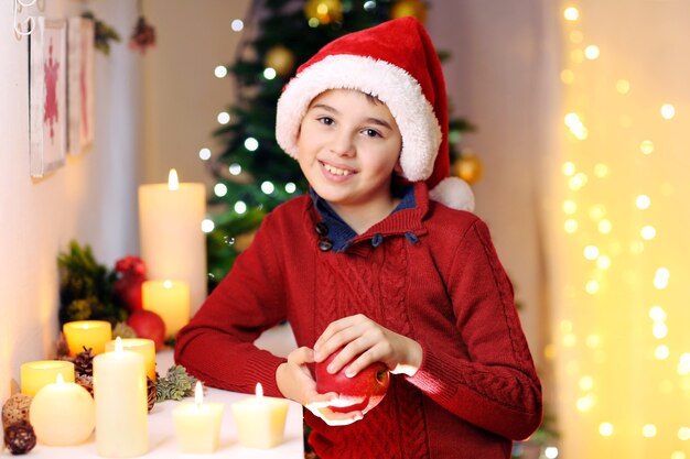 Petit garçon en bonnet de Noel près de la cheminée dans la chambre