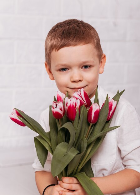 Petit garçon avec un bouquet de tulipes sur une surface blanche