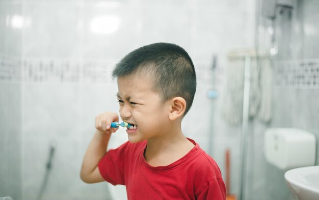 Photo petit garçon avec brosse à dents électrique sur fond de salle de bain gros plan soins dentaires souriant enfant heureux se brosser les dents avec une brosse à dents hygiène dentaire du petit garçon