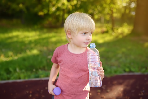 Petit garçon buvant de l&#39;eau pendant l&#39;entraînement avec des haltères